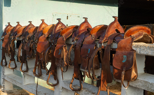 Fotografie leather western trail saddles with saddle bags and horns lined up on white fence