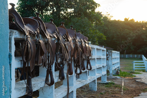 leather western trail saddles with saddle bags and horns lined up on white fence in rural Cuba saddle bags marked with letters horizontal format shot before horse back riding adventure in rural Cuba photo