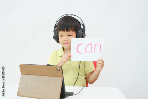 Little Asian child using tablet pc studying online lesson at home, Kid learn to read via e-learning , English lesson, Kindergarten closed during Covid-19 health crisis, Distance learning concept photo