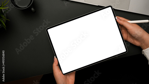 Female hands holding tablet and stylus pen over black office desk.