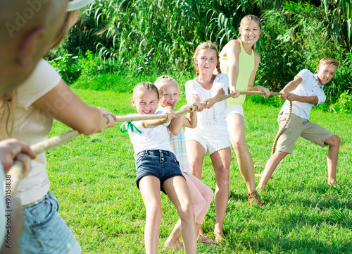 Group of laughing people with smiling active kids having fun together outdoors pulling rope
