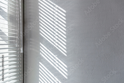 sunlight through a window of blinds. shadows on the white stucco wall.
