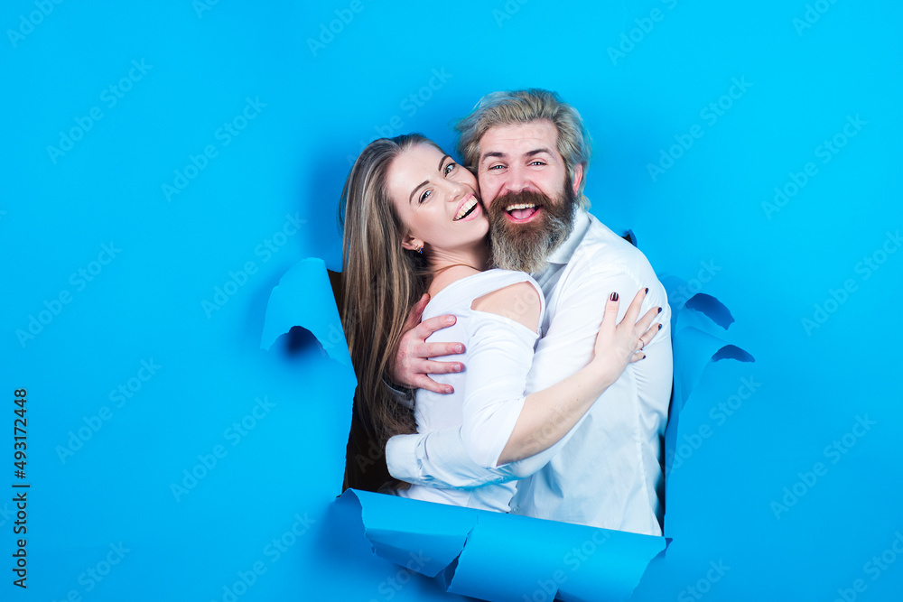 Couple through hole in blue paper. Discount and sale, people hole background. Surprised couple of man and woman making hole in paper looking through hole. Advertising board, blue background. Couple through hole in blue paper. Discount and sale, people hole background. Surprised couple of man and woman making hole in paper looking through hole. Advertising board, blue background.
