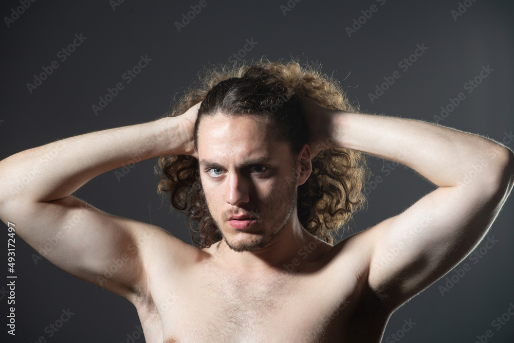 Young man with curly hair. Handsome man combing hair. Man with bare nude torso and curly hair.