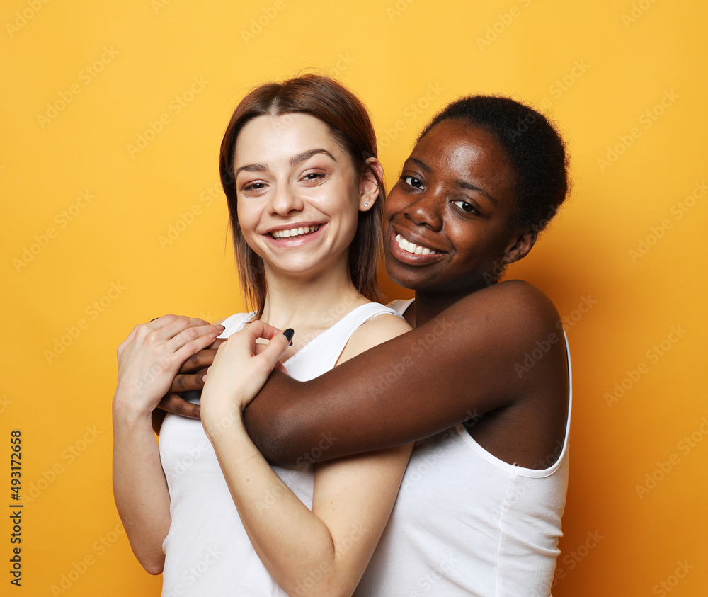 Close-up portrait of two multiracial females over yellow background. Close-up portrait of two multiracial females over yellow background.