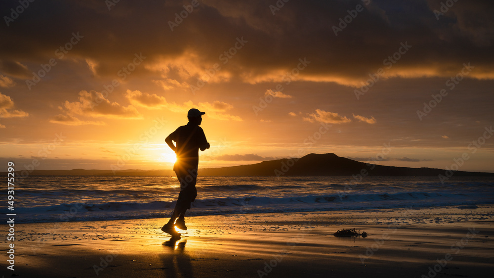 Silhouette man running on Milford beach at sunrise, Rangitoto Island in the background, Auckland.