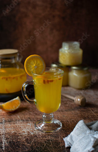 Glass mug with a drink of sea buckthorn, lemon and honey on a wooden background. Image with copy space, vertical orientation, side view.