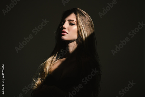 Sensual girl with art shadow light. Sensual woman with light on a black background. Beautiful female face in the darkness. Tender and seductive look. Fashion art studio portrait.