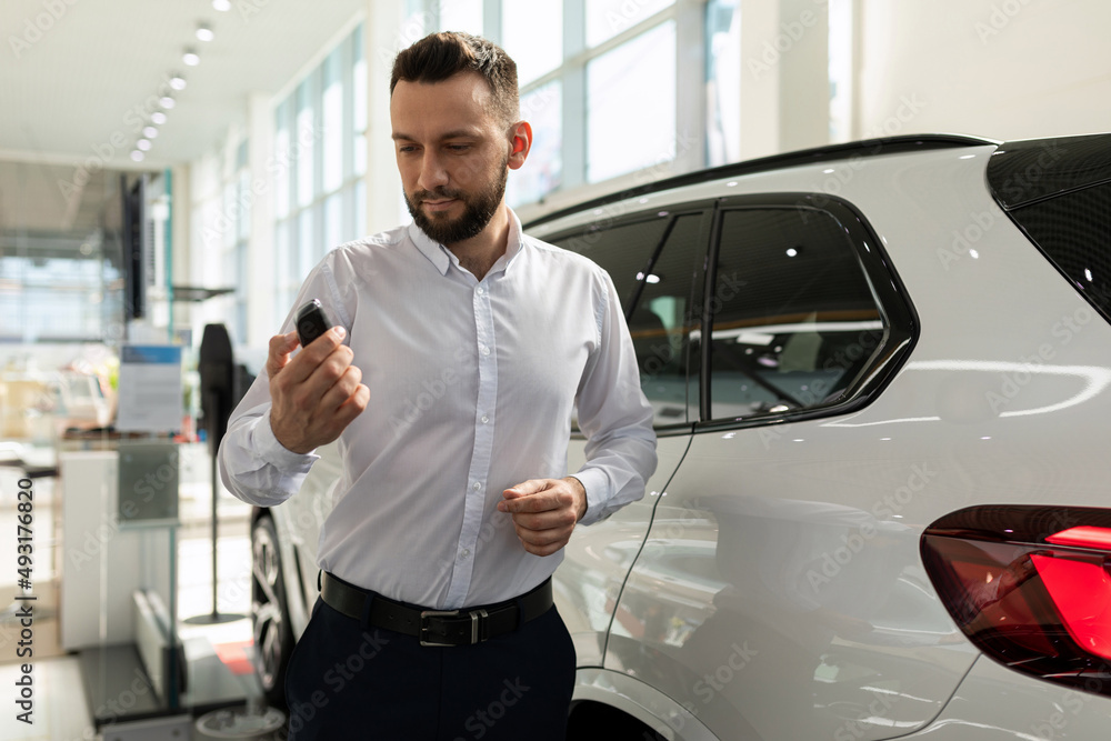a man in a white shirt in a car dealership is turned on in his hands next to a white SUV a man in a white shirt in a car dealership is turned on in his hands next to a white SUV