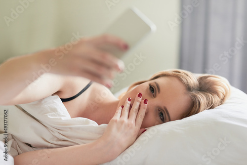 Checking out her social media feeds. Shot of an attractive young woman texting on her cellphone while lying in her bed at home.