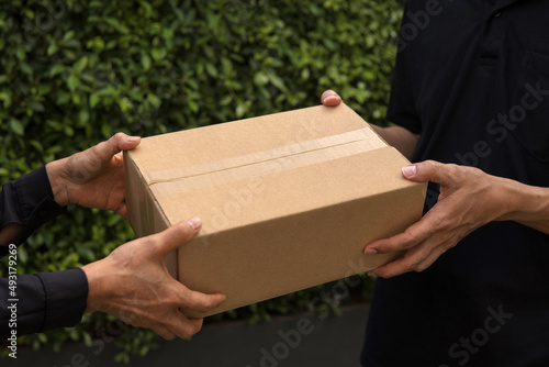 Closeup Man's hand taking blank recycled paper cardboard box shopping from woman with outdoor green leaves nature garden background. Delivery boxes mockup for branding design concept