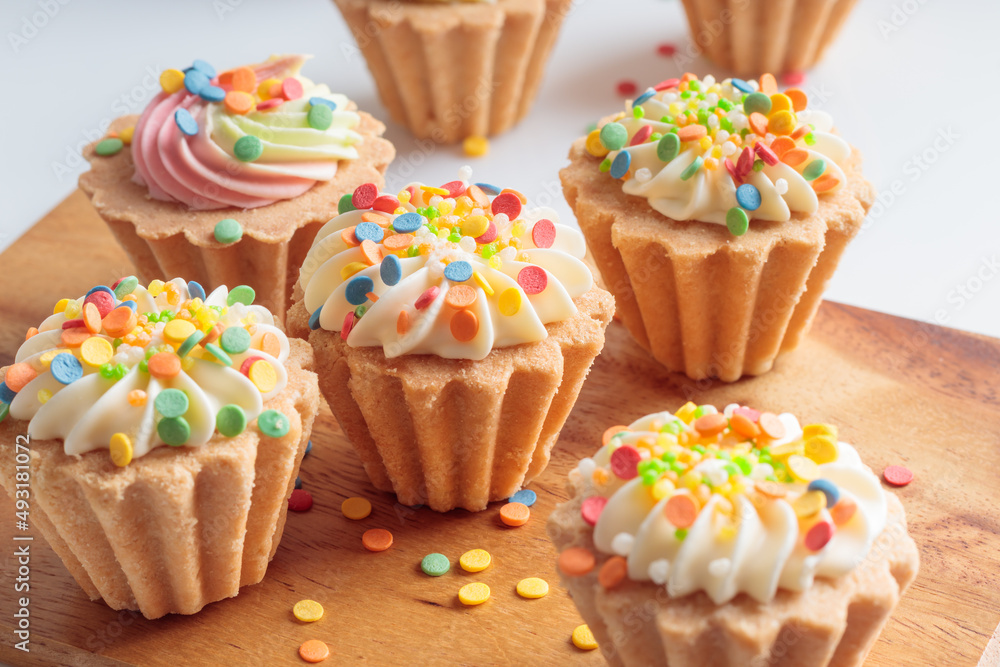 Close-up view of mini cupcakes decorated with candy sprinkles on wooden background. Soft focus.