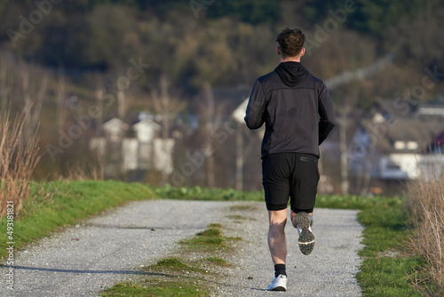 Mann in kurzer Hose und Kapuzenjacke joggt auf einem Feldweg photo