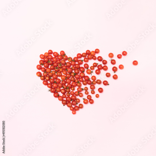 A cherry tomatoes shaped into a heart falls apart in pieces on pastel pink background. Minimal fruit and love concept. Flat lay with copy space