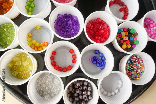 Beads of various colors are placed in a white plastic glass.