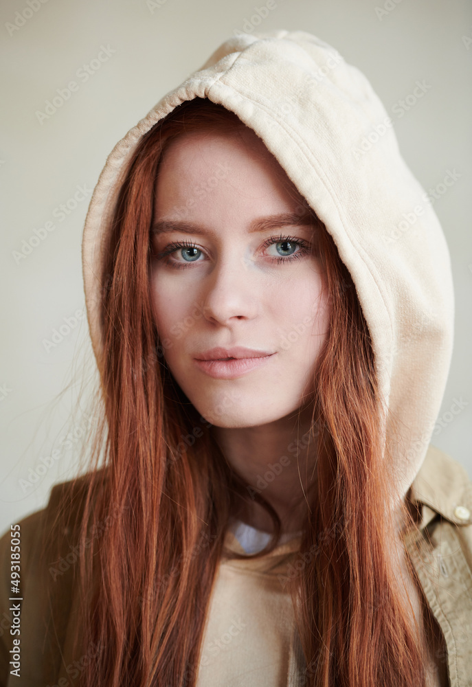 Vertical close-up portrait shot of attractive young Caucasian woman with red hair and gray eyes wearing hood looking at camera