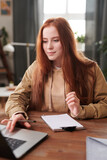 Vertical medium portrait of beautiful young female college student sitting at desk at home focusing on doing homework
