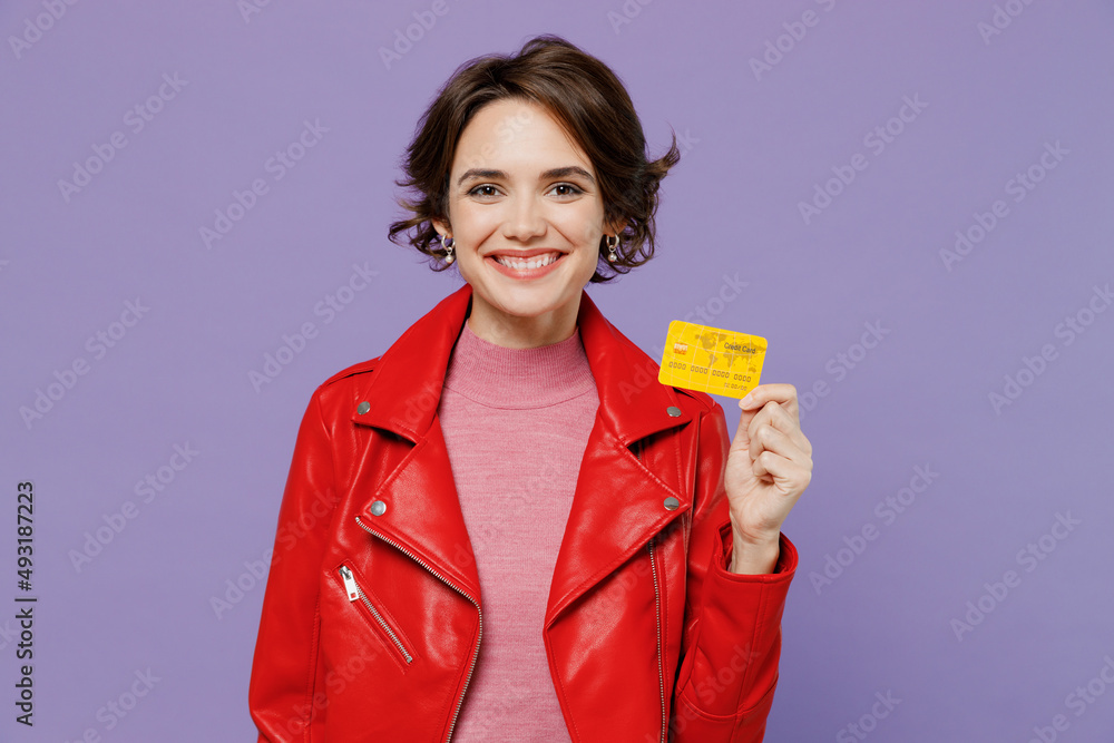 Young smiling happy rich satisfied woman 20s wear red leather jacket hold in hand credit bank card isolated on plain pastel light purple background studio portrait. People lifestyle fashion concept. Young smiling happy rich satisfied woman 20s wear red leather jacket hold in hand credit bank card isolated on plain pastel light purple background studio portrait. People lifestyle fashion concept.