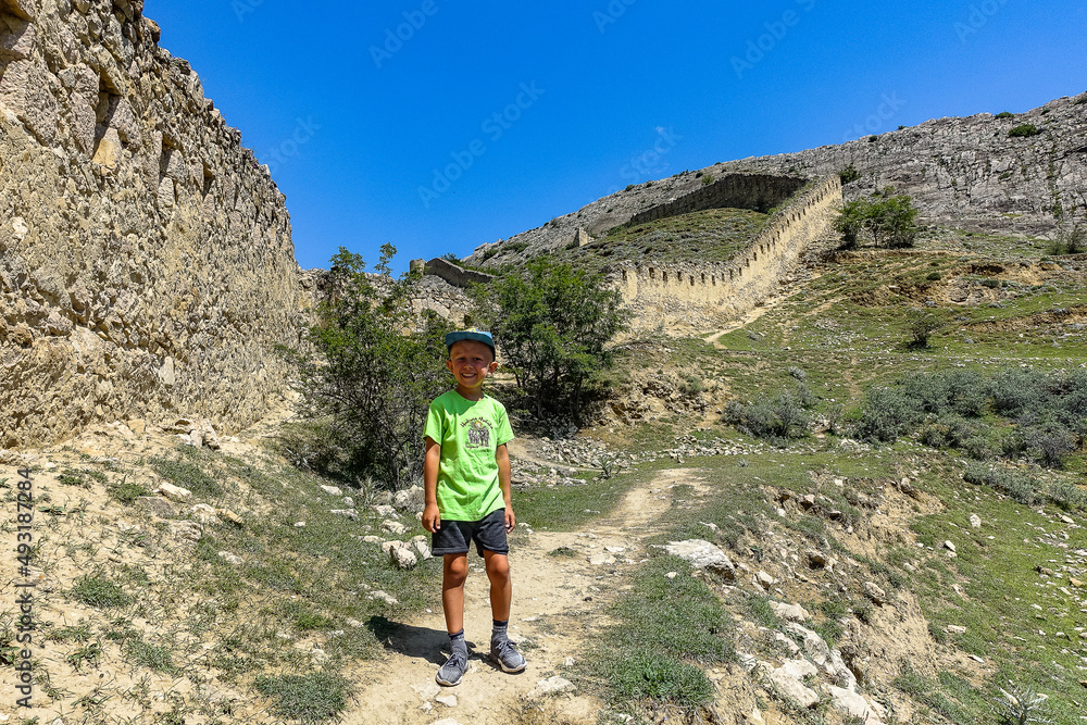 A boy against the background of the Gunib fortress. A protective wall. Russia, Dagestan. June 2021