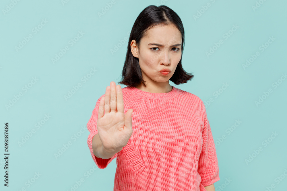 Young strict serious sad woman of Asian ethnicity 20s wearing pink sweater showing stop gesture with palm isolated on pastel plain light blue color background studio portrait People lifestyle concept Young strict serious sad woman of Asian ethnicity 20s wearing pink sweater showing stop gesture with palm isolated on pastel plain light blue color background studio portrait People lifestyle concept