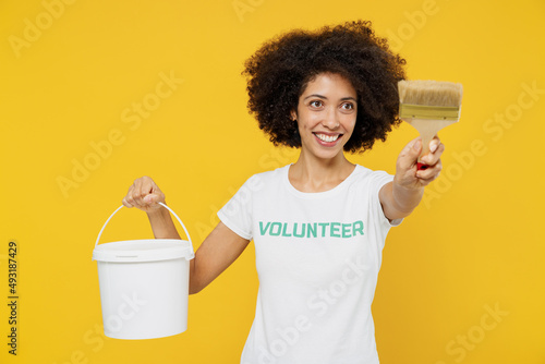 Foto Young fun woman of African American ethnicity in white volunteer t-shirt hold paint bucket brush working isolated on plain yellow background