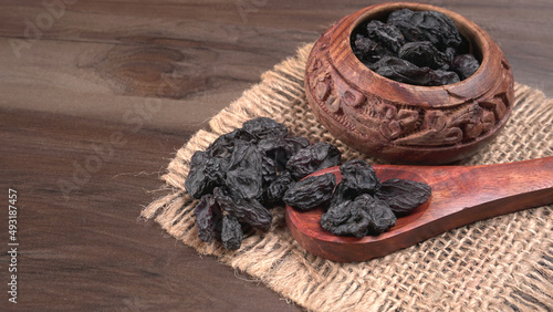 black raisins in a bowl on a wooden table. black raisins in a spoon