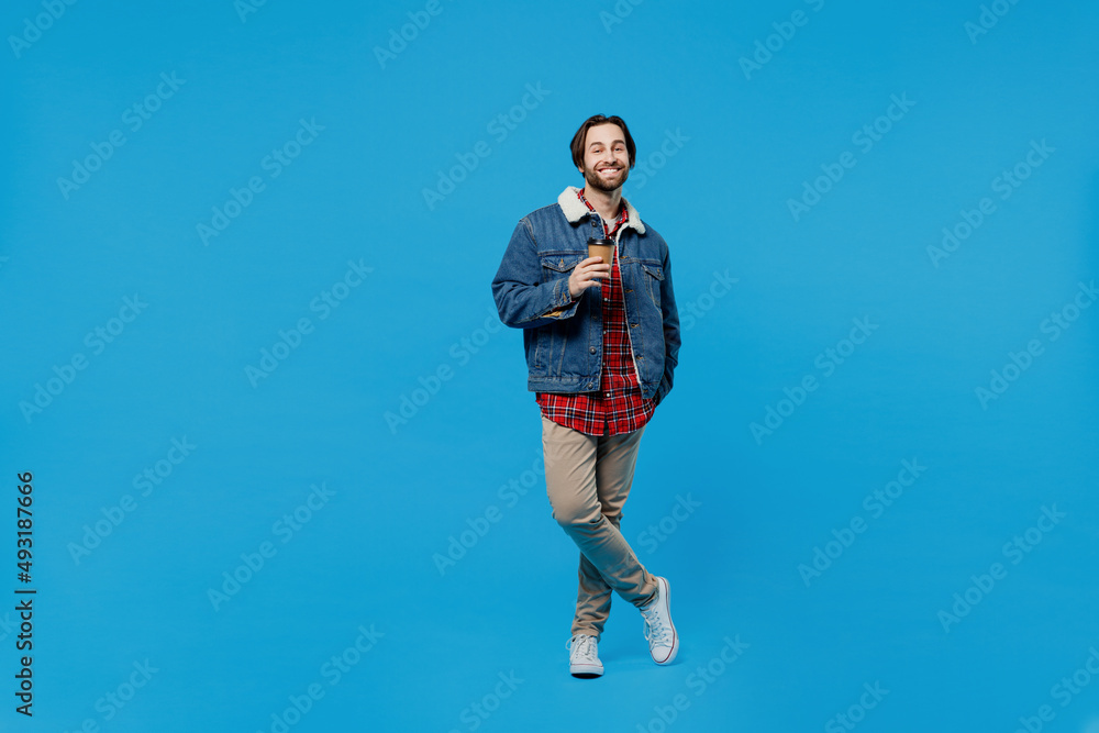 Full size young brunet bearded man 20s in denim jacket hold takeaway delivery craft paper brown cup coffee isolated plain pastel light blue background studio portrait. Winter cold season concept Full size young brunet bearded man 20s in denim jacket hold takeaway delivery craft paper brown cup coffee isolated plain pastel light blue background studio portrait. Winter cold season concept