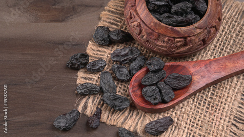 black raisins in a bowl on a wooden table. black raisins in a spoon