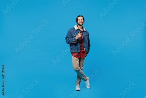 Full size young brunet bearded man 20s in denim jacket hold takeaway delivery craft paper brown cup coffee isolated plain pastel light blue background studio portrait. Winter cold season concept