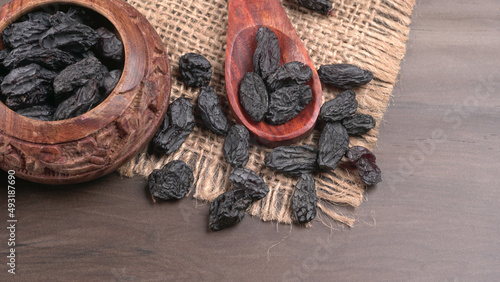 black raisins in a bowl on a wooden table. black raisins in a spoon