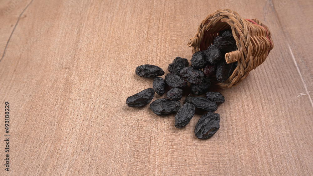 black raisins in a bowl on a wooden table. black raisins in a spoon black raisins in a bowl on a wooden table. black raisins in a spoon