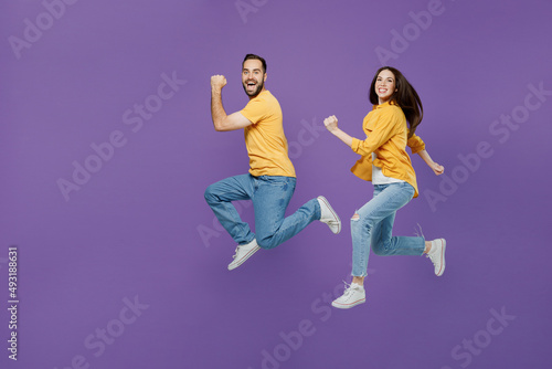 Full size young excited cheerful fun overjoyed couple two friends family man woman together in yellow casual clothes jump high run fast hurry up isolated on plain violet background studio portrait