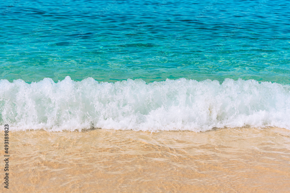 Summer scene with blue sea water, white foam and yellow sand close up with selective focus. Vacation or holiday concept. Nature background with copy space