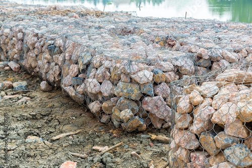 Stone walls, protection from backshore erosion. Stones in a metal mesh. Gabion wall constructed using steel wire mesh basket. Steel gabion filled with granite rocks at river bank. photo
