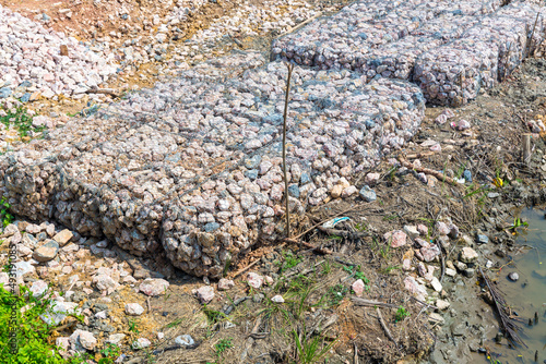 Stone walls, protection from backshore erosion. Stones in a metal mesh. Gabion wall constructed using steel wire mesh basket. Steel gabion filled with granite rocks at river bank. photo