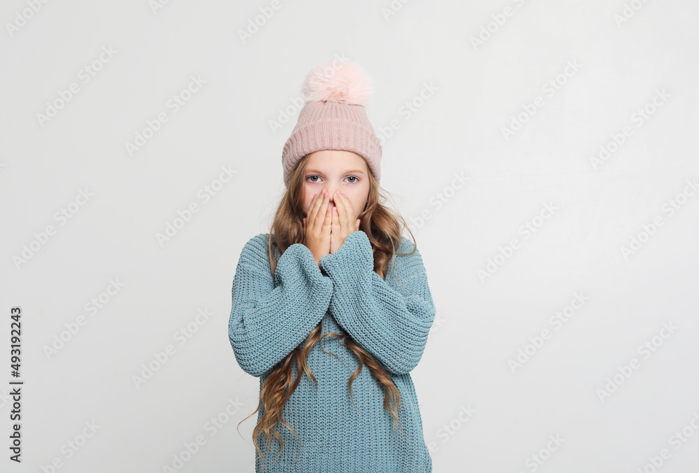 Little girl in a winter hat in surprise covered her mouth with her hand Little girl in a winter hat in surprise covered her mouth with her hand