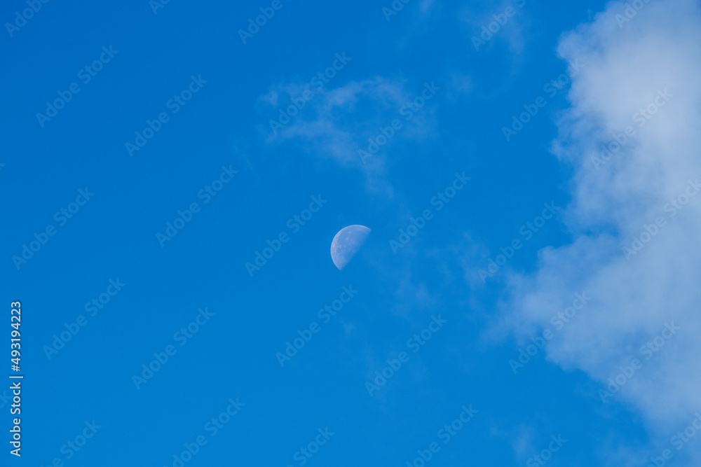 part of the moon during the day against the blue sky and clouds part of the moon during the day against the blue sky and clouds