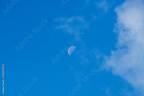 part of the moon during the day against the blue sky and clouds 