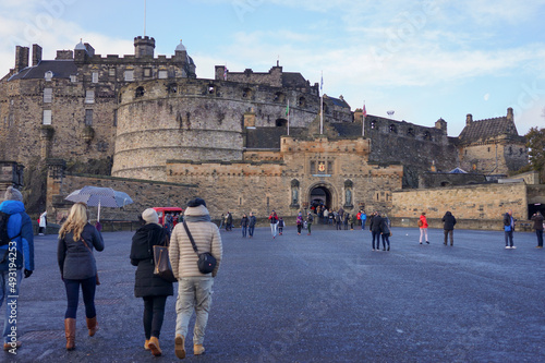View of the medieval Edinburgh castle front gate with crowd of people walking in morning with clouds in clear blue sky background.