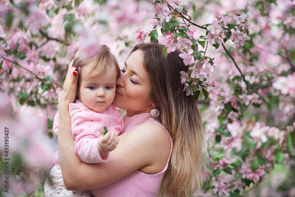 Little beautiful girl with her beautiful mother outdoors in blossom. Family daughter and mother kissing and embracing in street. Happy smart family in park Little beautiful girl with her beautiful mother outdoors in blossom. Family daughter and mother kissing and embracing in street. Happy smart family in park