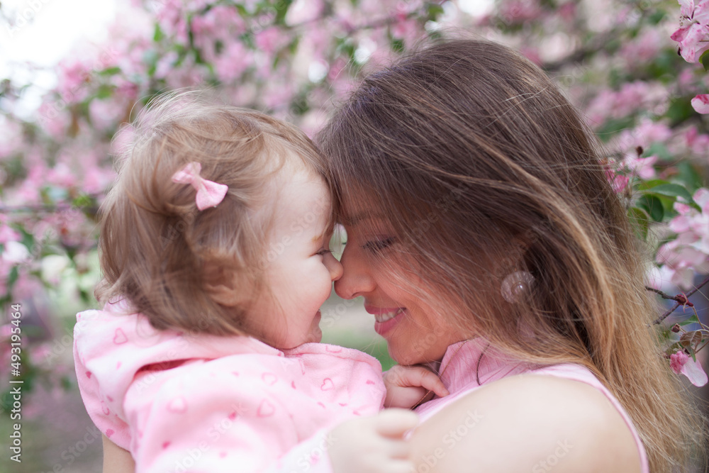 Little beautiful girl with her beautiful mother outdoors in blossom. Family daughter and mother kissing and embracing in street. Happy smart family in park Little beautiful girl with her beautiful mother outdoors in blossom. Family daughter and mother kissing and embracing in street. Happy smart family in park