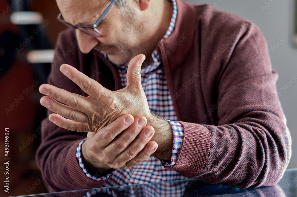 A middle-aged man is wincing and his left hand hurts because he has arthritis, rheumatism, osteoarthritis or osteoporosis. A middle-aged man is wincing and his left hand hurts because he has arthritis, rheumatism, osteoarthritis or osteoporosis.