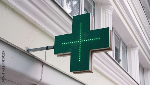 Flashing sign of the city pharmacy in the form of a cross with green glowing LED lamps. The concept of medicines, pandemics, rising drug prices, the quality of pharmacy products