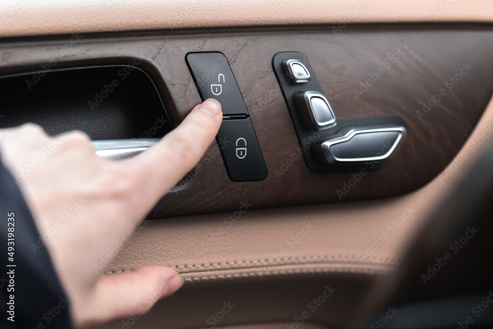 Hand with car door lock switch inside the luxury car interior with leather and wood design. Close-up view photo