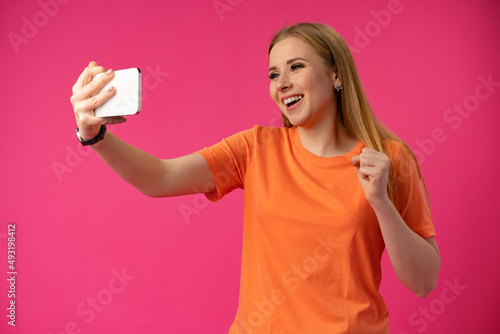 Happy woman taking selfie against studio color background