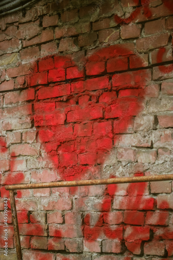 A big red heart painted on a red brick wall. Rough background with a symbol of love. Valentine's Day declaration of love on February 14. A big red heart painted on a red brick wall. Rough background with a symbol of love. Valentine's Day declaration of love on February 14.