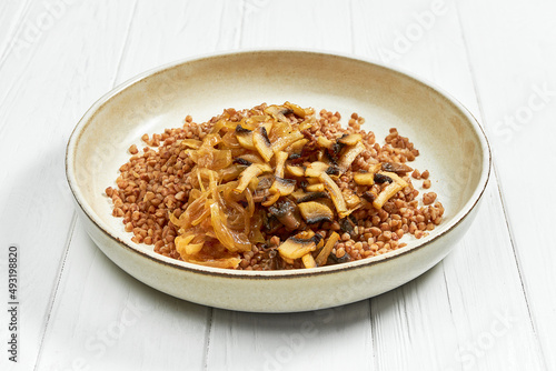 Buckwheat porridge with mushroom in a plate on a white wooden background
