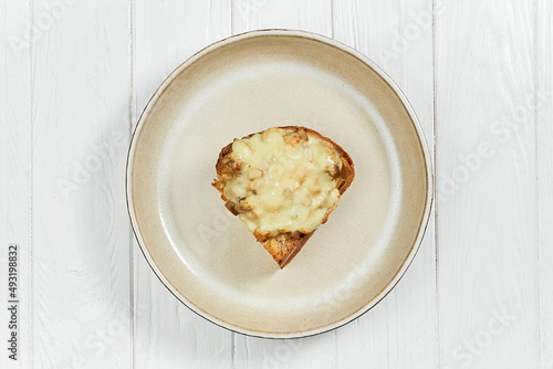 Toast with baked cheese and chicken in a plate on a white wooden background.