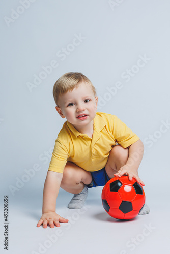 Cheerful little boy 5-6 years old football fan in a yellow T-shirt, supports the team, holds a soccer ball in his hands, isolated on a white background. The concept of sports family recreation