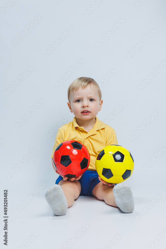 Little european boy, fan or player in yellow and blue uniform with a soccer ball, supports the soccer team on a white background. Football sport game, lifestyle concept. Isolated on white background Little european boy, fan or player in yellow and blue uniform with a soccer ball, supports the soccer team on a white background. Football sport game, lifestyle concept. Isolated on white background
